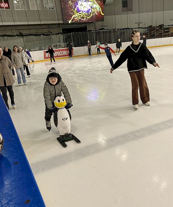 Маленький ребёнок учится кататься на коньках с помощью помогатора в виде пингвина