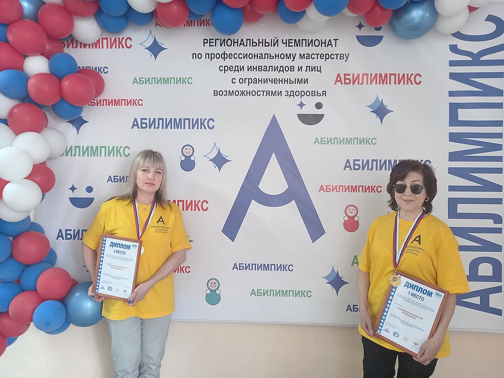 Две девушки в жёлтых футболках с медалями и дипломами стоят на фоне баннера Абилимпикса