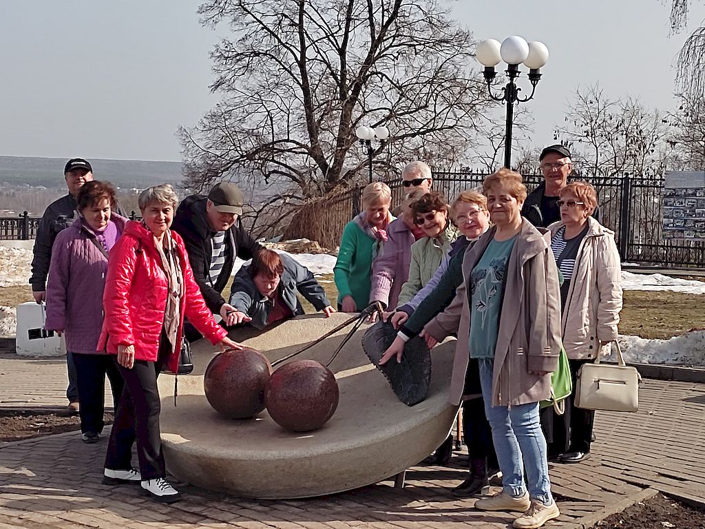 Участники поездки около памятника Владимирской вишне. Две ягоды с веткой между ними и листом лежат на круглой тарелке.