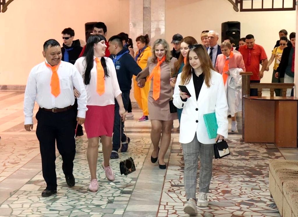 Участники слёта идут, взявшись за руки по несколько человек по холлу санатория. Многие улыбаются. Почти на всех одеты галстуки синего и оранжевого цвета.