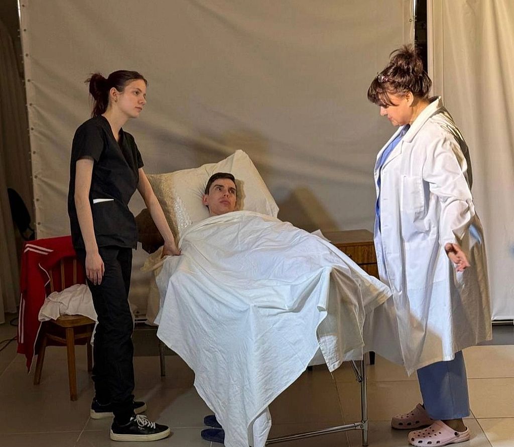 момент спектакля: мужчина лежит в больничной палате. Слева от него стоит девушка, справа - медсестра
