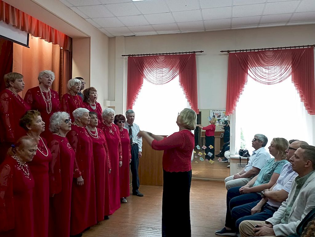 Выступление хора. Участницы одеты в бордовые платья в пол.