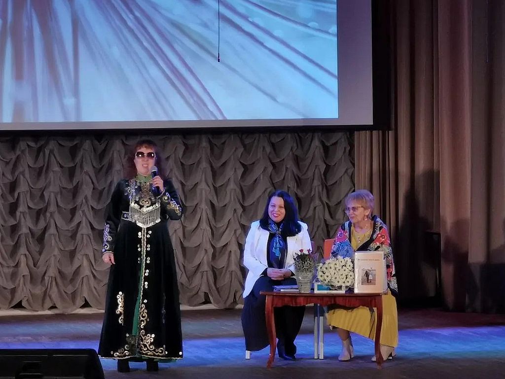 Лилия Ханипова исполняет песню - подарок. За ней на сцене сидят Н. Ш. Федорина и Г. Закирова