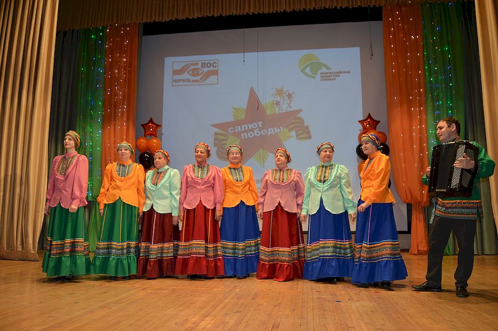На сцене участники фестиваля - восемь женщин в ярких юбках и кофтах и мужчина с аккордеоном
