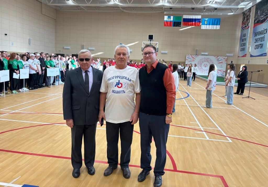 в спортивном зале на фоне большого количества спортсменов стоят трое мужчин