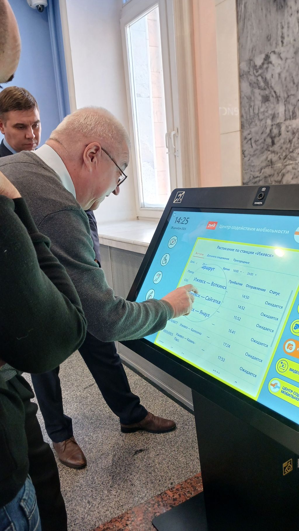 слабовидящий человек с помощью встроенной в монитор лупы смотрит расписание поездов 