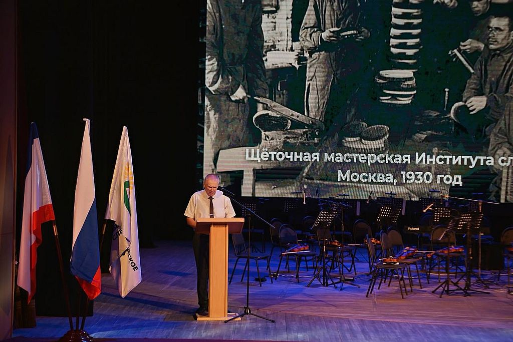 на сцене затрибуно стоит председатель Крымской РО ВОС. Рядом с ним флаг РФ и флаг ВОС