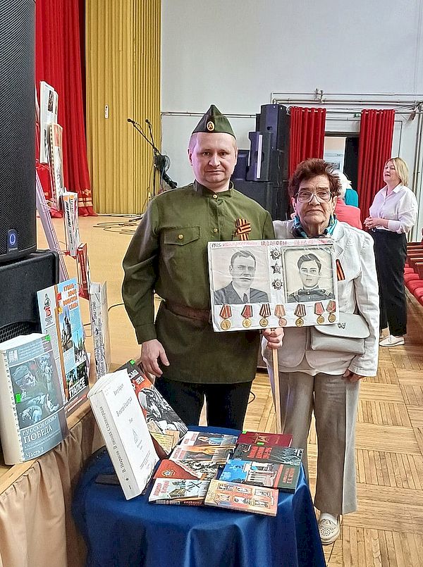 На фотографии мужчина в военной форме и женщина держат в руках фотографии своих родственников с медалями и орденами.