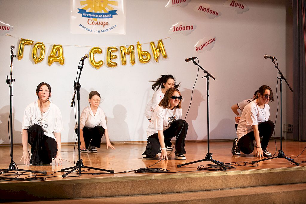 На фотографии на сцене дети танцуют. Они одеты в чёрные штаны и белые кофты