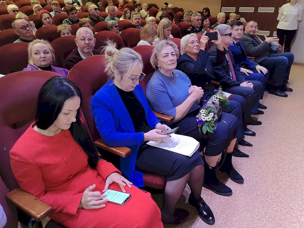 Зал. Крупным планом первый ряд с почетными гостями. В центре – директор Семейного центра имени А.И. Мещерякова с 2001 по 2024 год, Почетный гражданин Московской области Галина Епифанова в джемпере сиреневого цвета.   