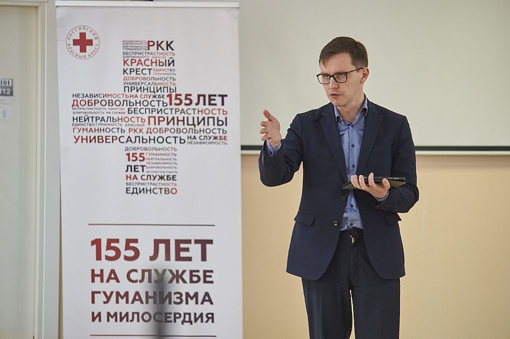 Мужчина в тёмно-синем костюме стоит рядом с баннером 