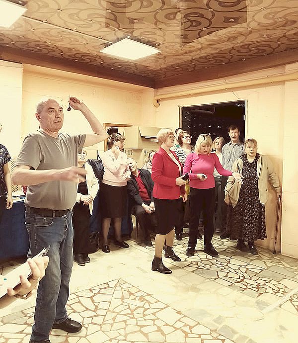 На фотографии мужчина с дротиком. Позади него участники и судьи соревнований.