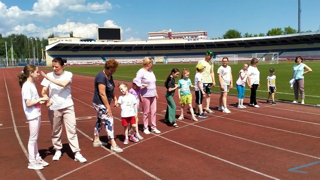 Дети - участники соревнований на старте беговой дорожки стадиона. Рядом с ними стоят женщины.