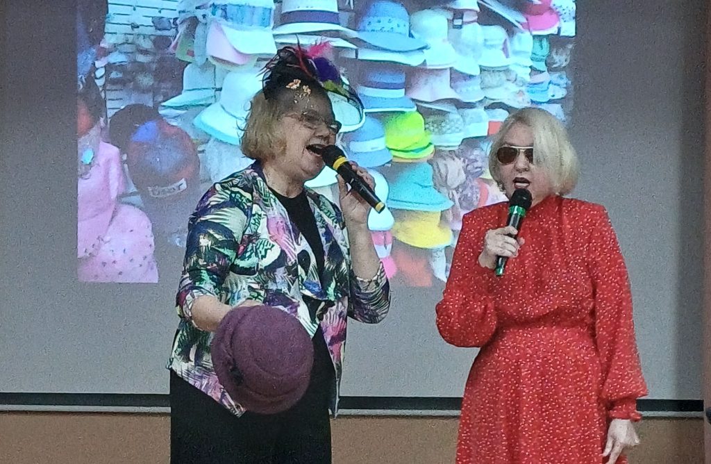 На сцене - ведущая и одна из конкурсанток в шляпе