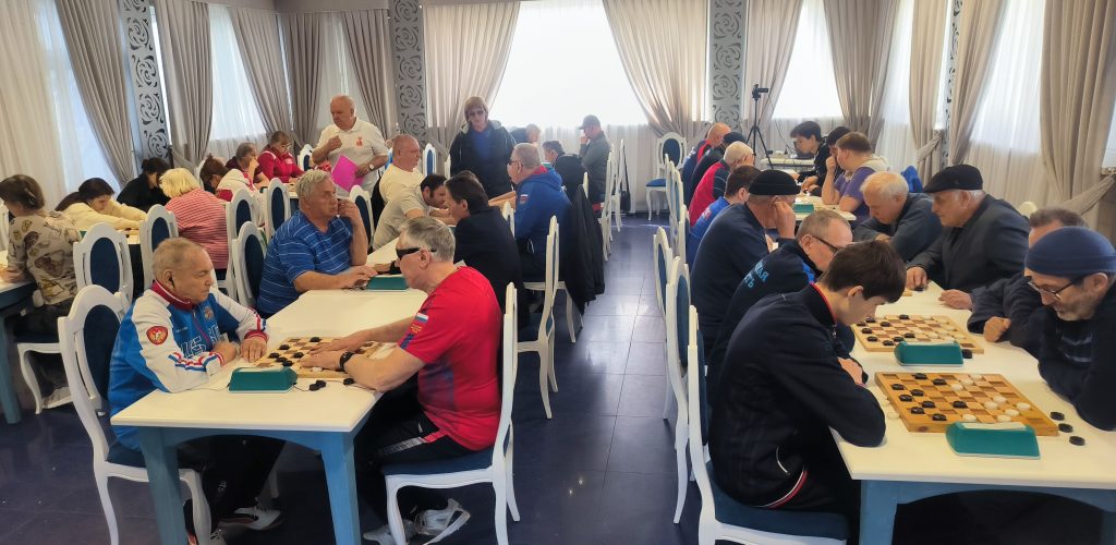 три длинных стола, за которыми  участники турнира играют в шашки