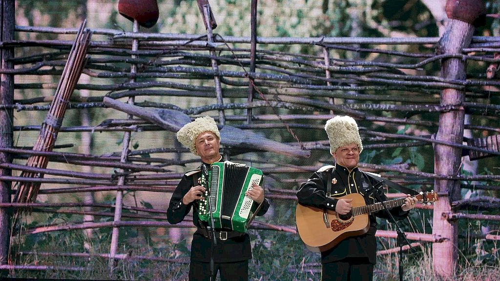 на сцене два исполнителя с гитарой и баяном. На голове надеты казачьи шапки