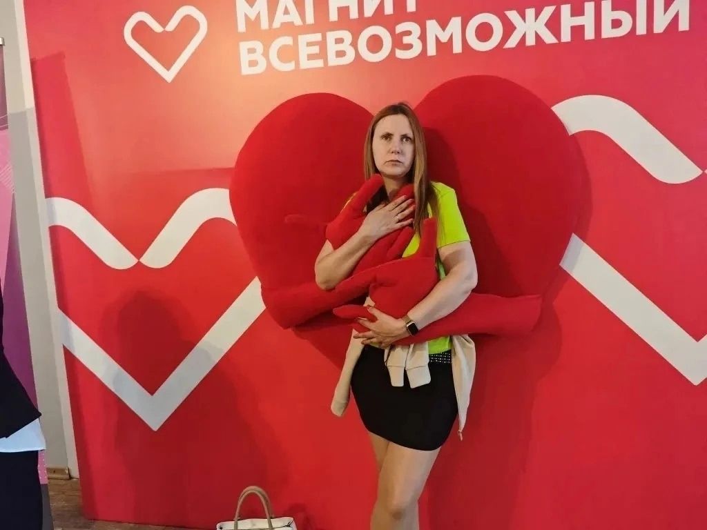 Анастасия Рыбушкина стоит на фоне красной стены с надписью