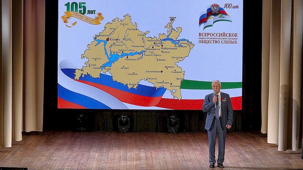 на сцене председатель Татарской РО ВОС Владимир Федорин. на заднике карта Татарстана, на которой отмечены города республики, где расположены местные организации