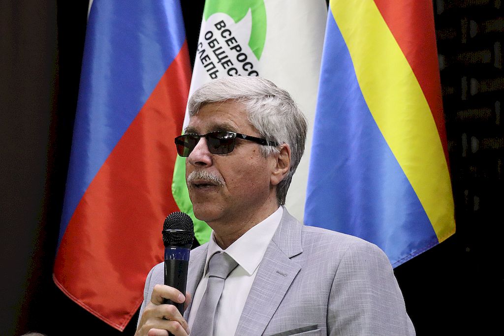 Владимир Храбан с микрофоном на фоне флагов РФ и ВОС