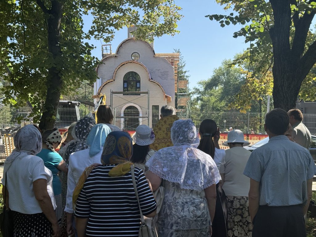 Прихожане и батюшка стоят лицом к строящемуся храму