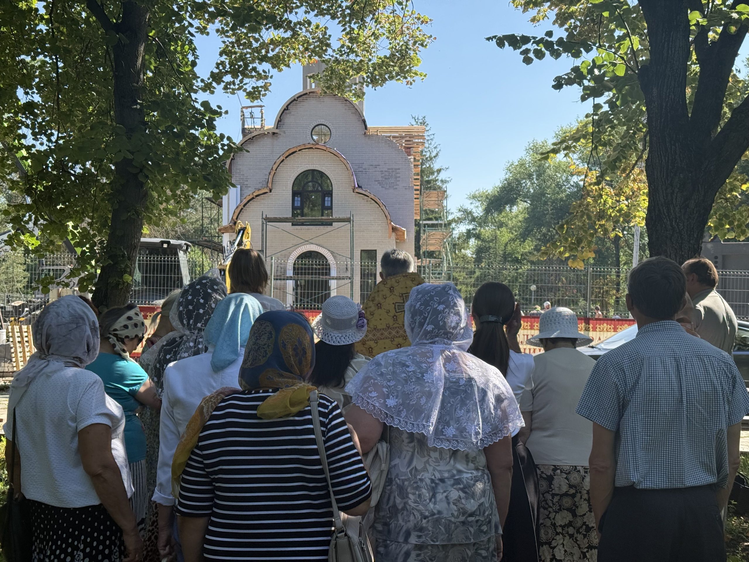 Прихожане и батюшка стоят лицом к строящемуся храму