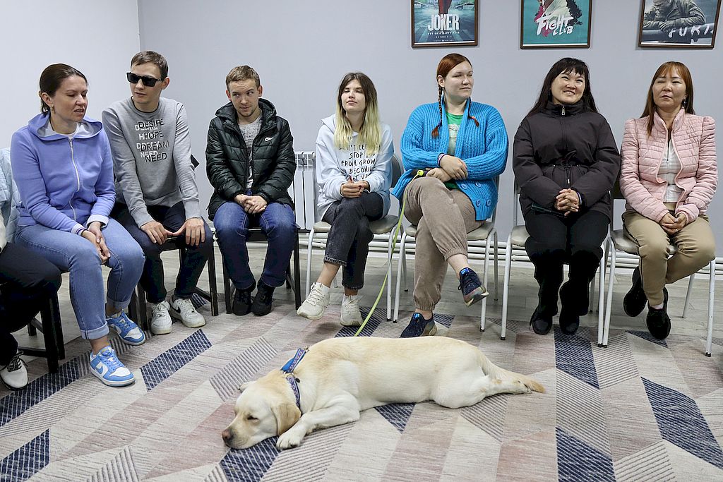 одна из площадок. Участники сидят на стульях, около их ног лежит собака-проводник