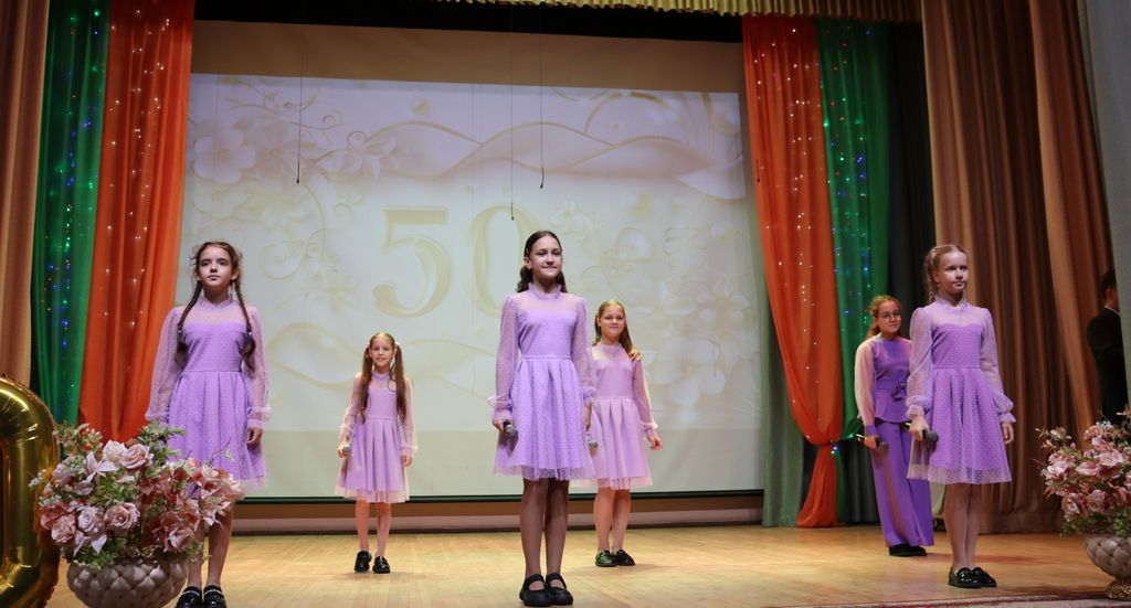 На сцене - девочки в сиреневых платьях и с микрофонами