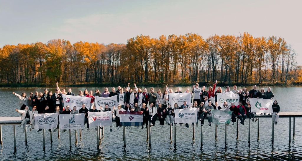 Участники лагеря сидят на мостках над водой с рекламными баннерами 